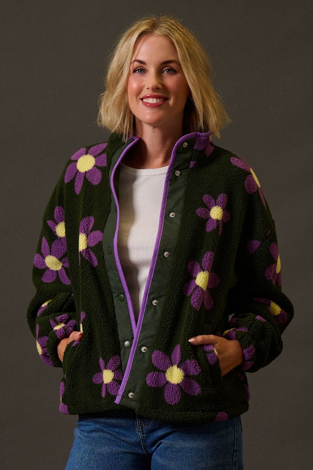 Woman wearing a dark green jacket with purple and yellow floral patterns on a brown background