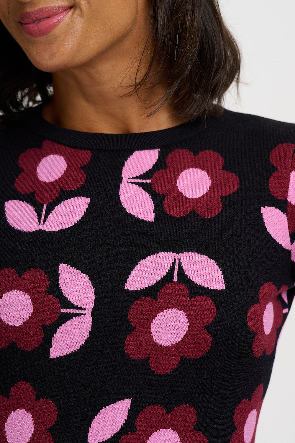 Close-up of a person wearing a black knit top with a repeating floral pattern in pink and burgundy.