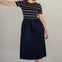 Sugarhill Brighton model wearing a black dress with colourful stripes and pink shoes against a plain background