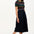 Sugarhill Brighton model wearing a black dress with colourful stripes and pink shoes against a plain background