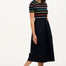 Sugarhill Brighton model wearing a black dress with colourful stripes and pink shoes against a plain background