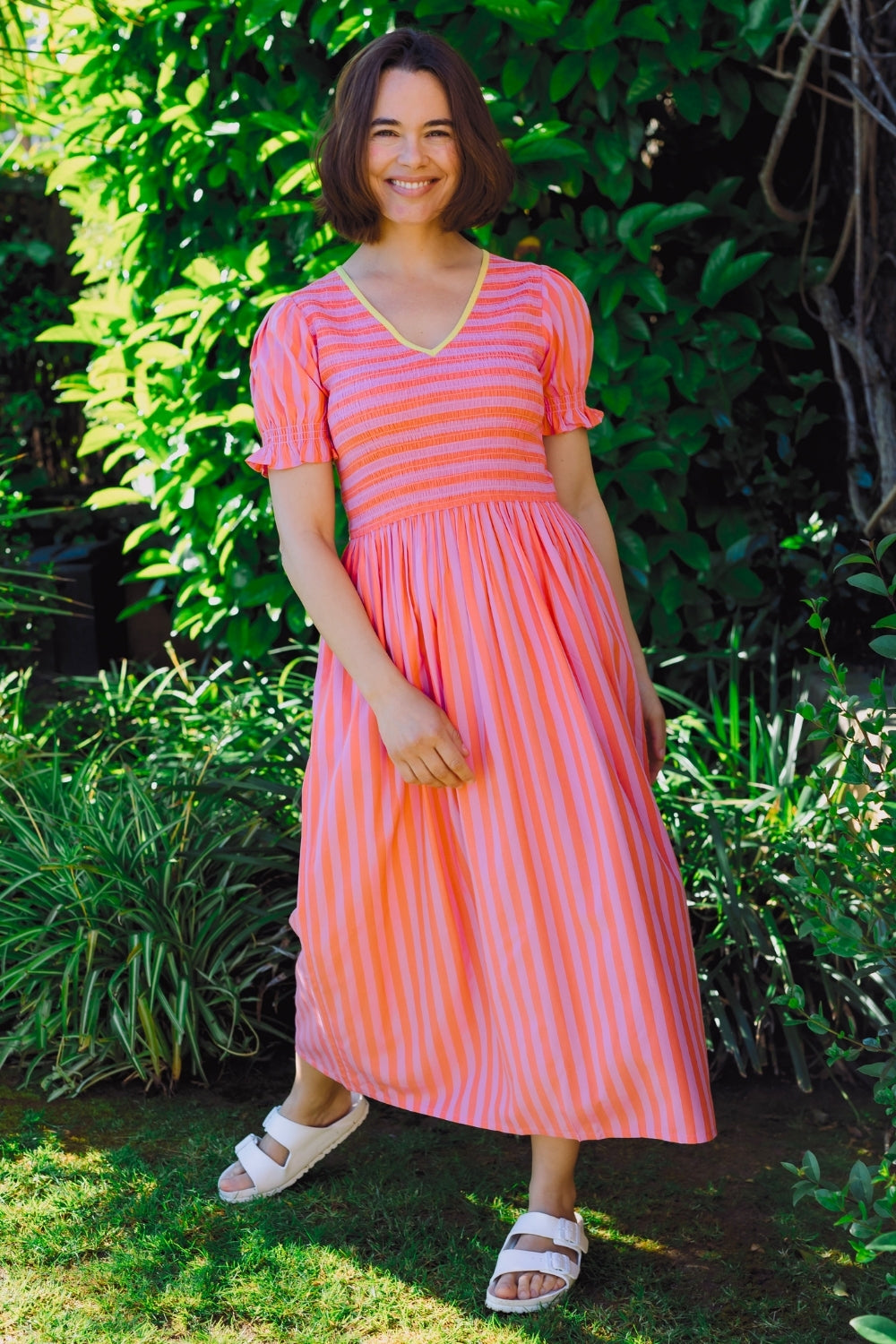 Woman wearing a pink and orange striped dress standing in a garden.