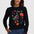 A woman wearing a black crewneck sweater with a colorful embroidered duck and floral design, paired with blue jeans, against a light gray studio background.