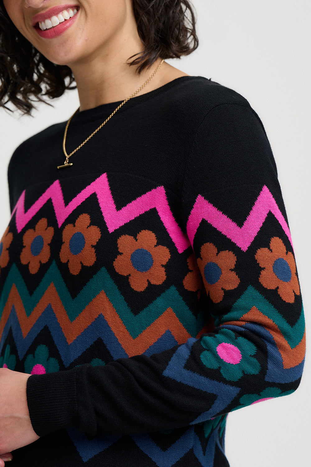 Person wearing a black sweater with colorful zigzag and floral pattern on a white background