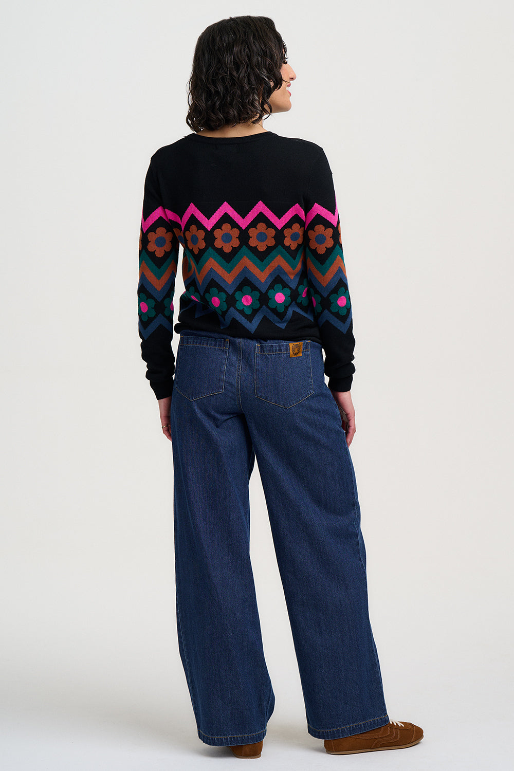 Person wearing a black sweater with colorful patterns and blue jeans on a white background