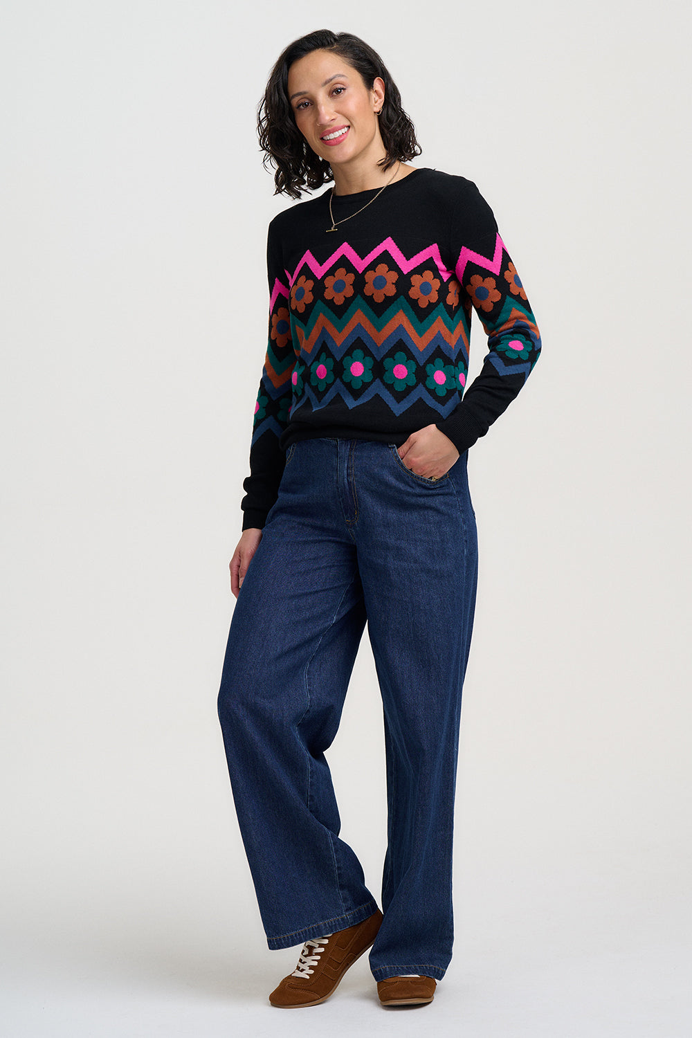 Woman wearing a colorful sweater with a zigzag pattern and blue pants on a white background