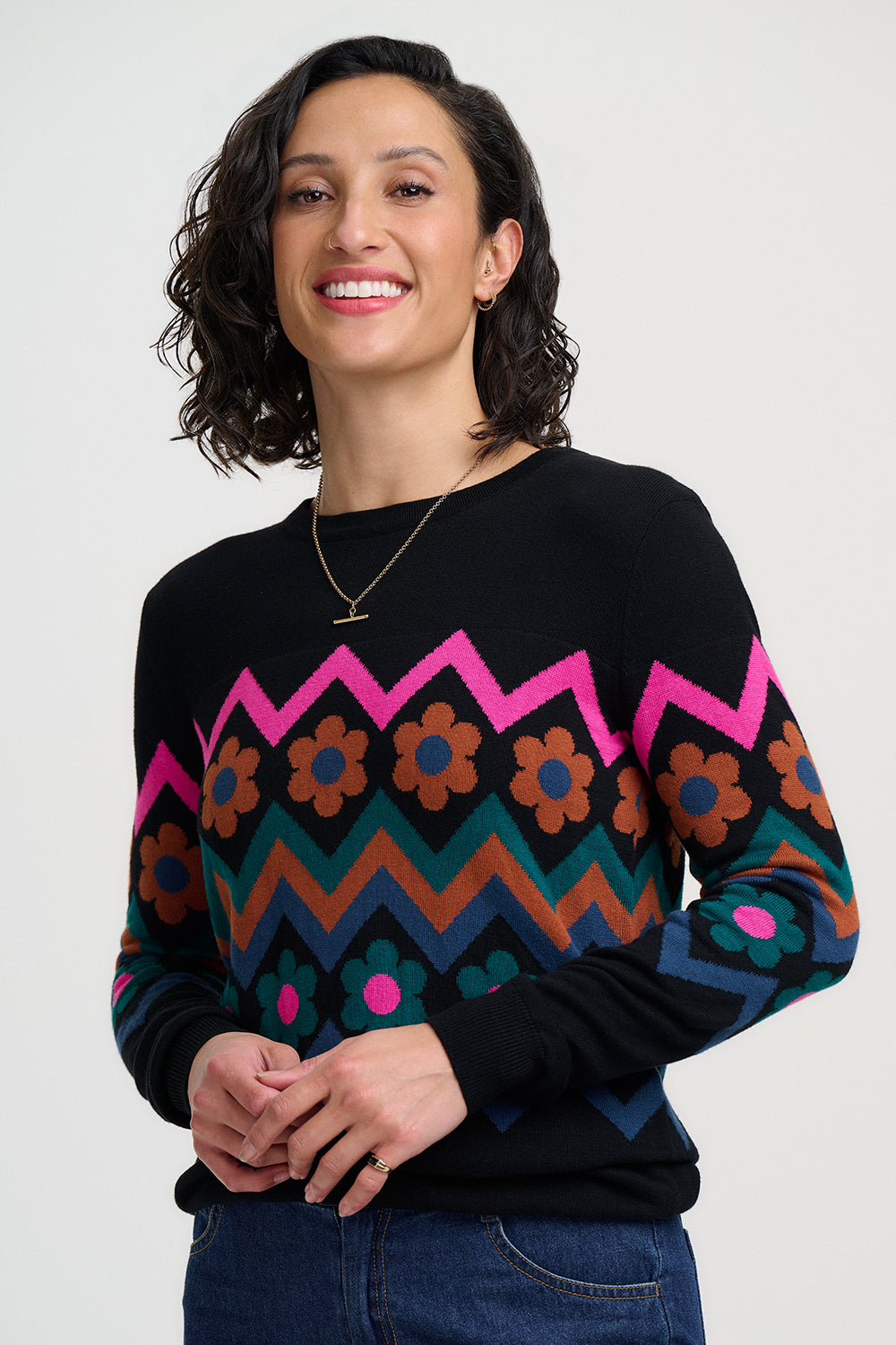 Woman wearing a black sweater with colorful zigzag and floral pattern on a white background