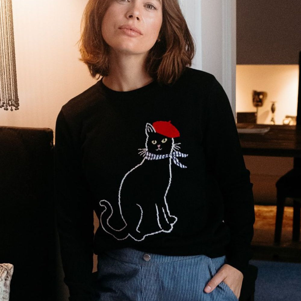 Person wearing a black sweater with a cat design, sitting indoors.