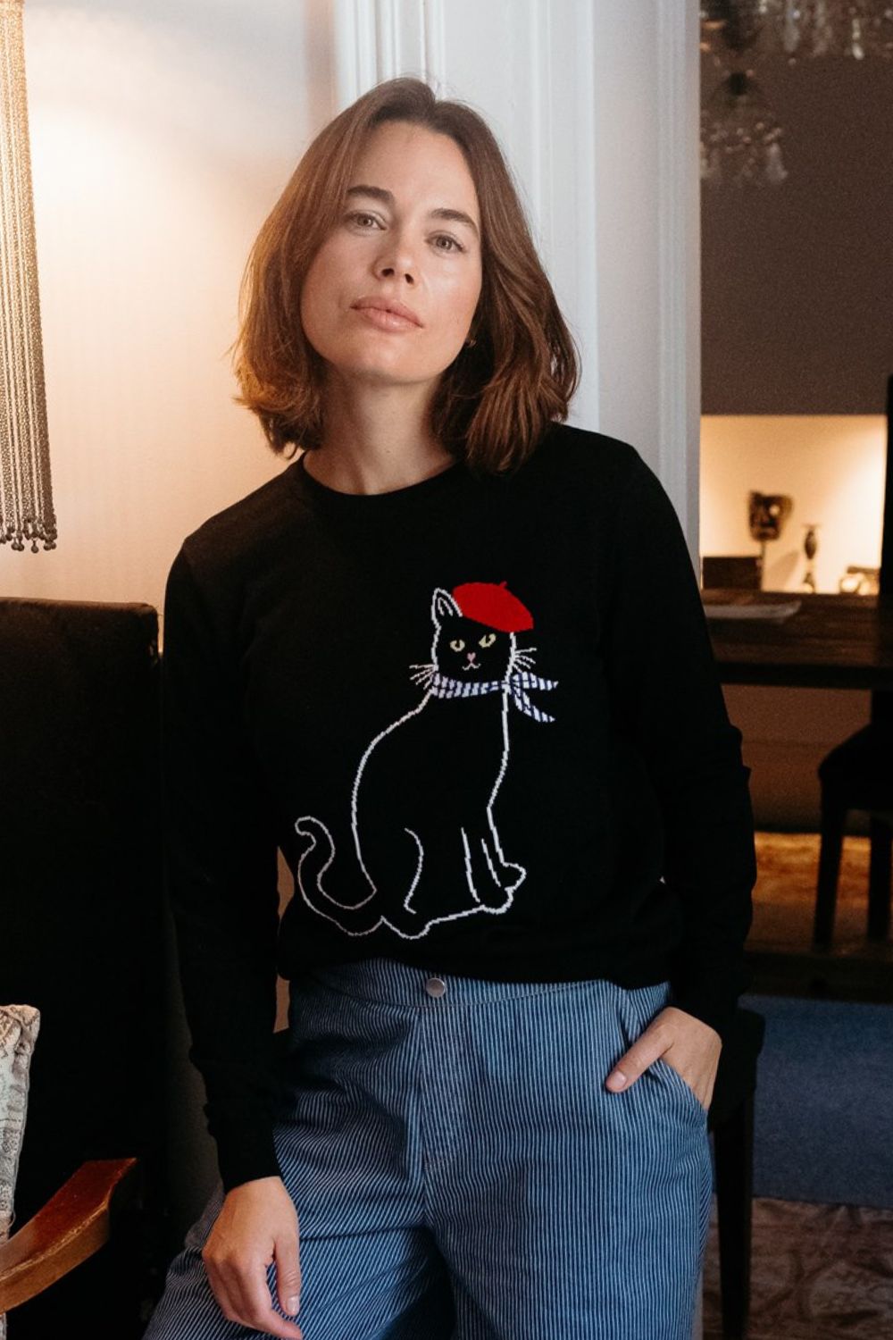 Person wearing a black sweater with a cat design, sitting indoors.