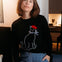 Person wearing a black sweater with a cat design, sitting indoors.