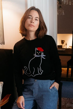 Person wearing a black sweater with a cat design, sitting indoors.