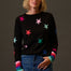 Woman wearing a black sweater with colorful star patterns against a dark background