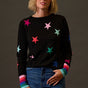 Woman wearing a black sweater with colorful star patterns against a dark background