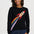 A woman wearing a black crewneck sweatshirt with a colorful rocket ship graphic on the front, paired with blue jeans, against a plain light gray background.