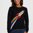 A woman wearing a black crewneck sweatshirt with a colorful rocket ship graphic on the front, paired with blue jeans, against a plain light gray background.