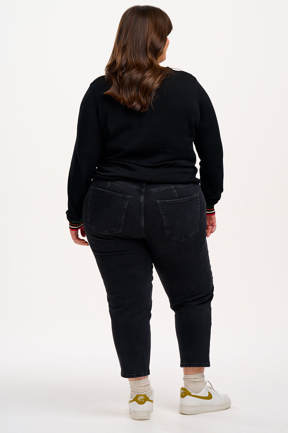 Person wearing a black sweater and blue jeans on a white background