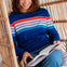 Woman in a striped sweater reading a book in a wicker chair.