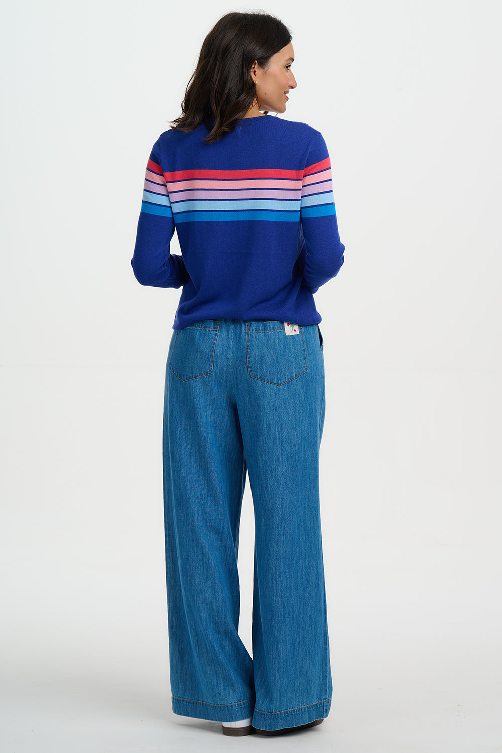 Woman wearing a blue sweater with colorful stripes and blue jeans on a white background