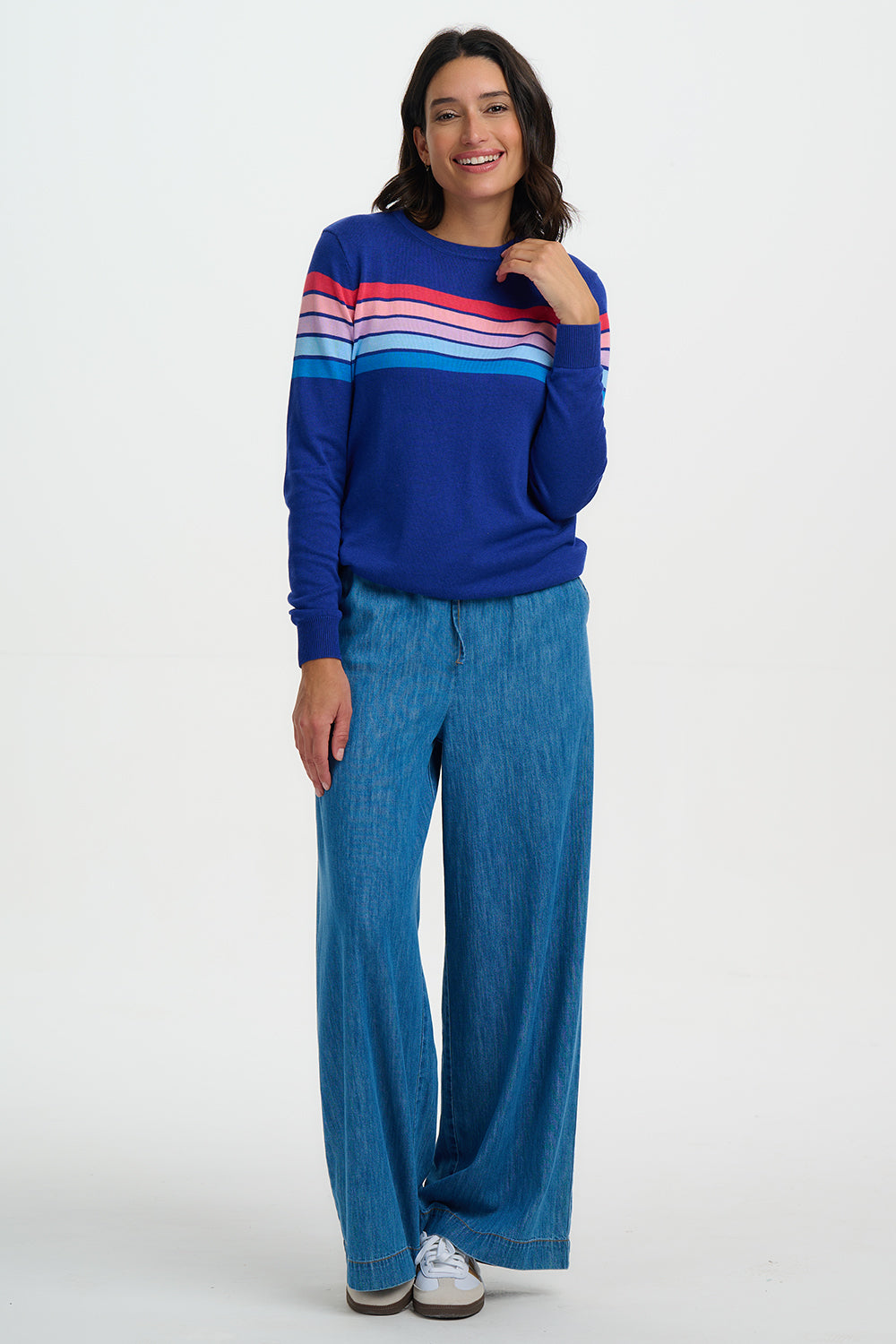 Woman wearing a blue sweater with colorful stripes and blue pants on a white background