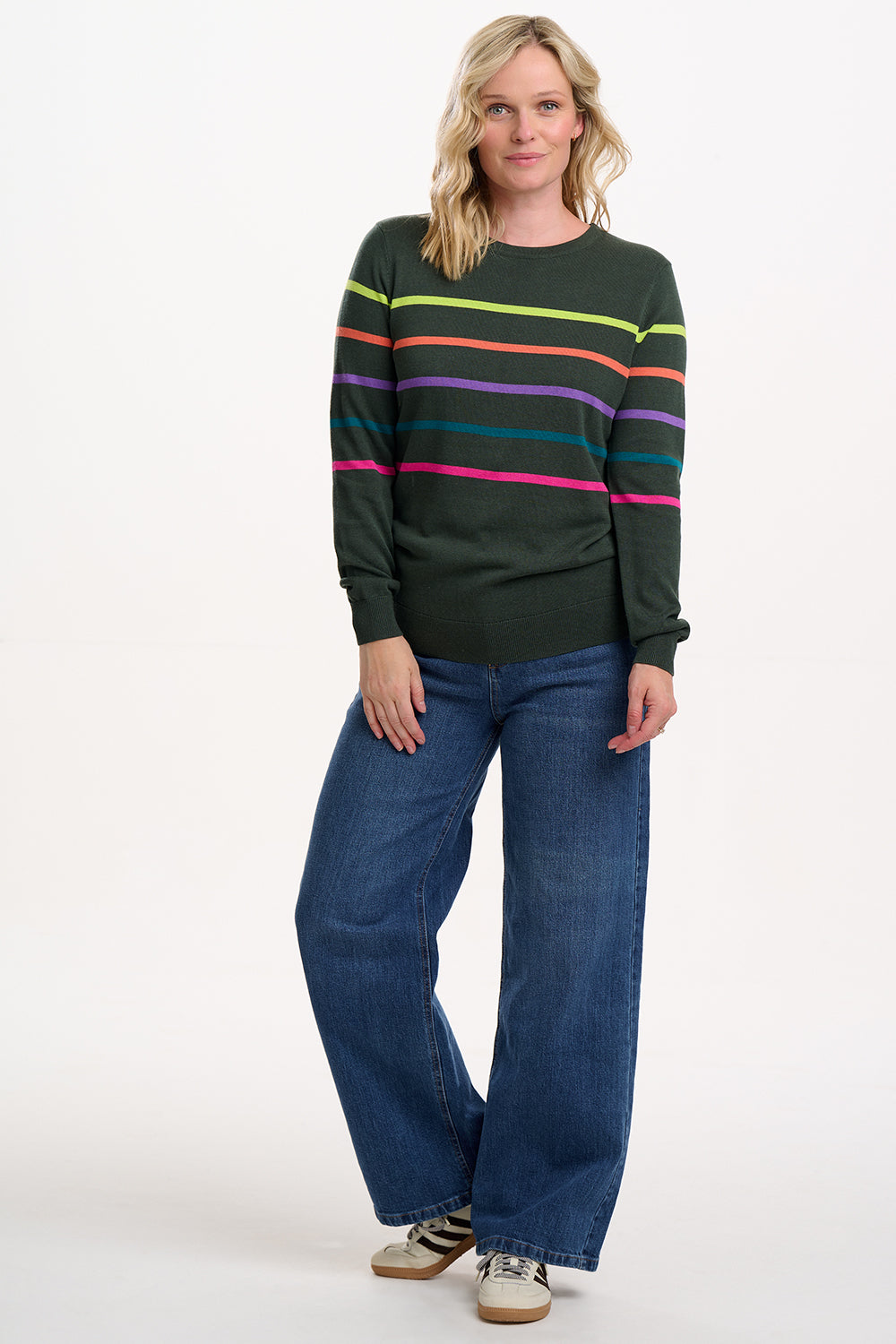 Woman wearing a dark green sweater with colorful stripes and blue jeans on a white background