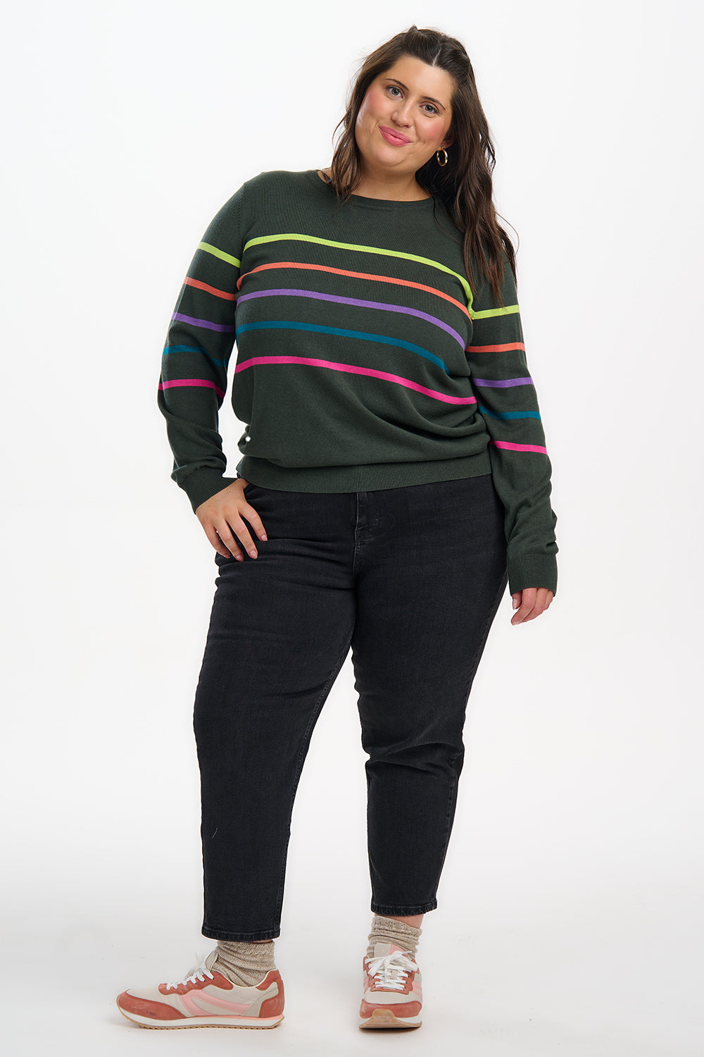 Woman wearing a green sweater with colorful stripes and black pants on a white background