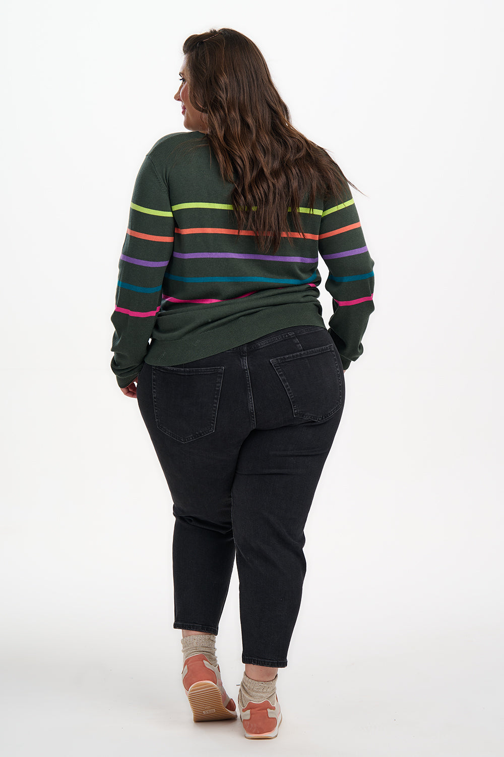Person wearing a green sweater with colorful stripes and black pants on a white background