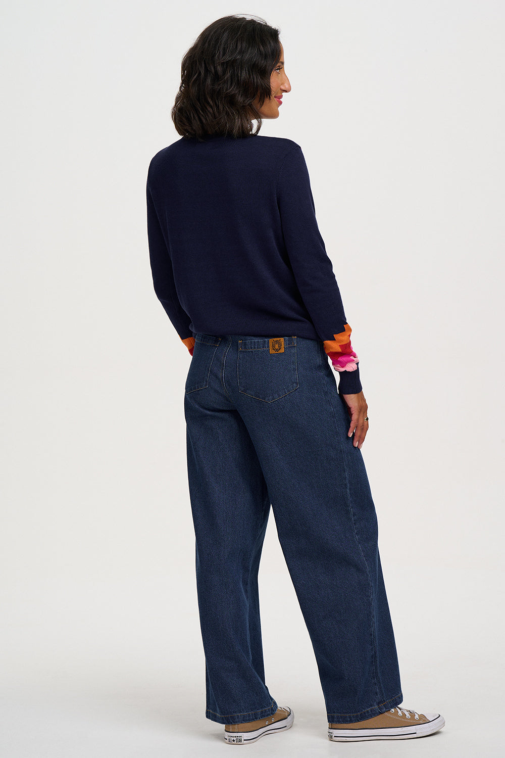 A model shown from the back wearing a navy blue long-sleeve top, dark blue wide-leg jeans, and brown canvas sneakers against a plain white studio background.