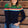 A woman wearing a navy and green color-blocked jumper with a rainbow split design across the chest, paired with blue jeans.