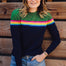 A woman wearing a navy and green color-blocked jumper with a rainbow split design across the chest, paired with blue jeans.