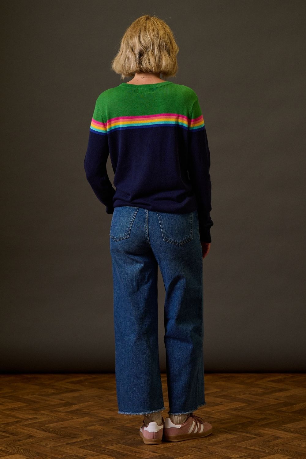 Person wearing a colorful striped sweater and blue jeans standing against a plain background