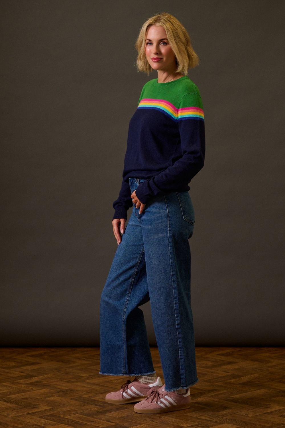 Woman wearing a colorful sweater and blue jeans against a dark background