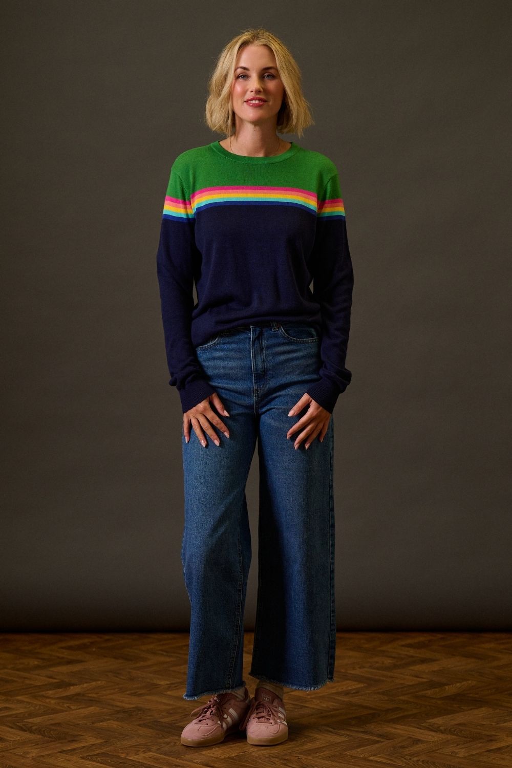 Woman wearing a colorful sweater and blue jeans against a dark background