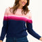 Sugarhill Brighton model wearing a navy jumper with pink gradient stripes, paired with jeans, standing against a white background.
