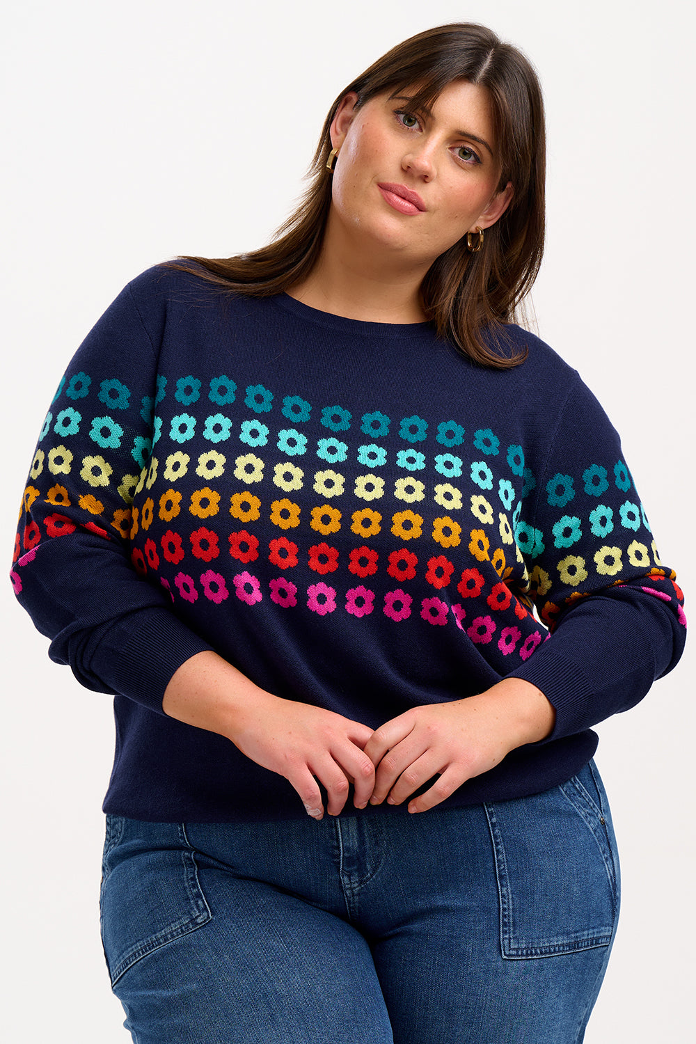 Sugarhill Brighton model wearing a navy blue jumper with a colourful geometric flower pattern, paired with jeans.