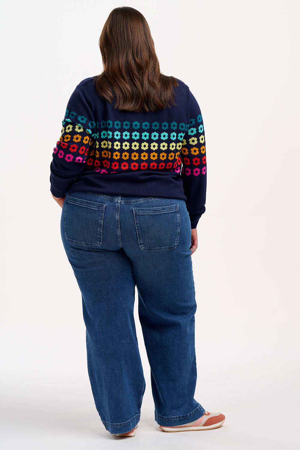 Sugarhill Brighton model wearing a navy blue jumper with a colourful geometric flower pattern, paired with jeans.