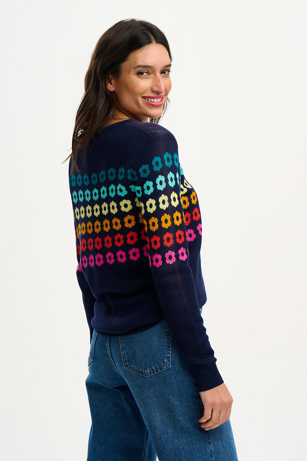 Sugarhill Brighton model wearing a navy blue jumper with a colourful geometric flower pattern, paired with jeans.
