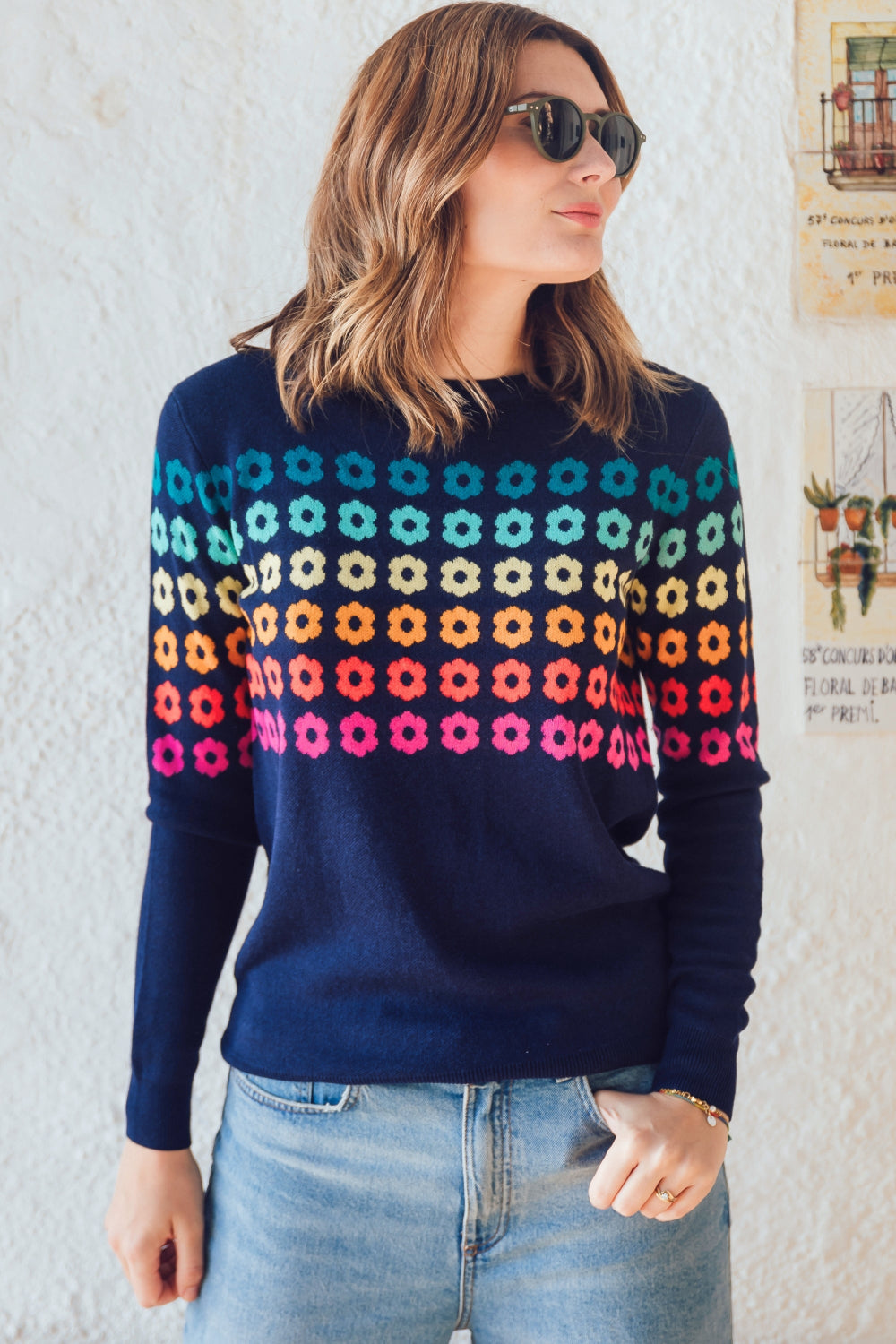 Sugarhill Brighton model wearing a navy blue jumper with a colourful geometric flower pattern, paired with jeans.