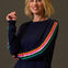 Woman wearing a navy sweater with colorful stripes on a brown background
