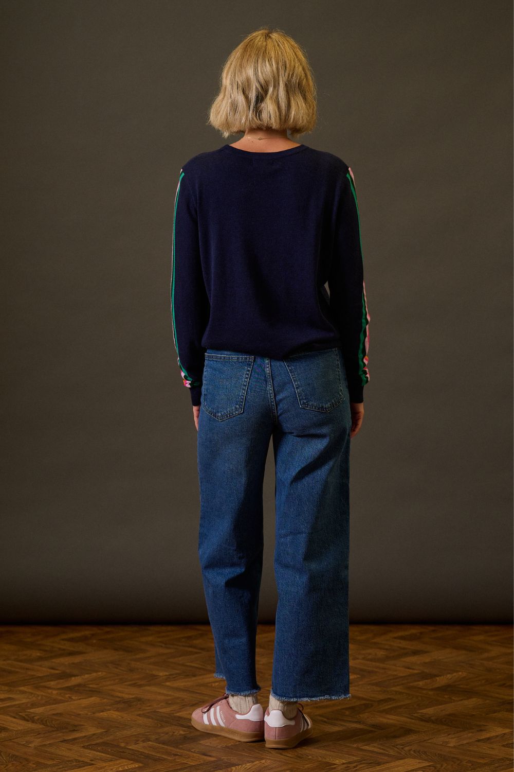 Person wearing a navy sweater and blue jeans standing against a plain background