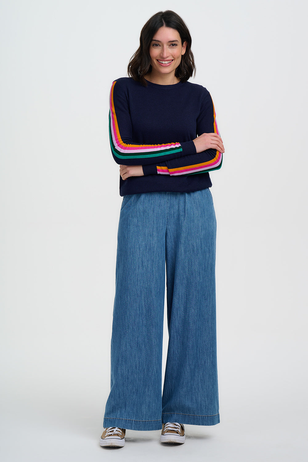 Person wearing a navy sweater with colorful stripes and blue jeans on a white background