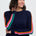 Person wearing a navy sweater with colorful stripes and blue jeans on a white background