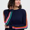 Person wearing a navy sweater with colorful stripes and blue jeans on a white background