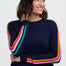 Person wearing a navy sweater with colorful stripes and blue jeans on a white background
