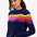 Sugarhill Brighton model wearing a navy blue jumper with horizontal retro stripe bands in pink, yellow, and other colours across the chest and shoulders.