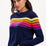 Sugarhill Brighton model wearing a navy blue jumper with horizontal retro stripe bands in pink, yellow, and other colours across the chest and shoulders.