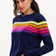 Sugarhill Brighton model wearing a navy blue jumper with horizontal retro stripe bands in pink, yellow, and other colours across the chest and shoulders.