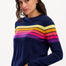 Sugarhill Brighton model wearing a navy blue jumper with horizontal retro stripe bands in pink, yellow, and other colours across the chest and shoulders.