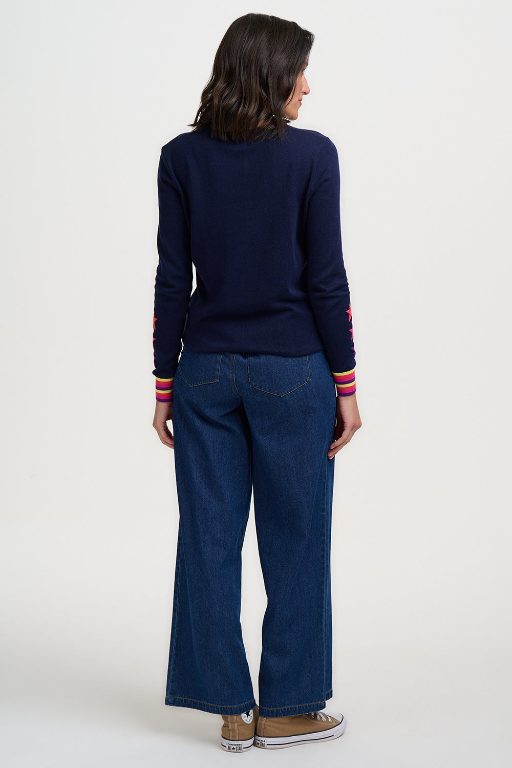 Person wearing a navy sweater with colorful cuffs and hem, paired with blue jeans on a white background