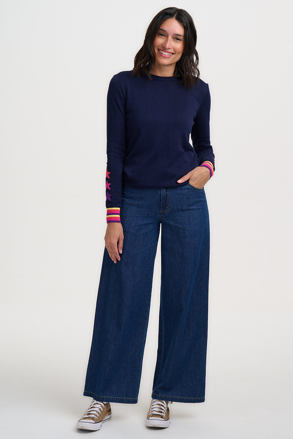 Woman wearing a navy sweater and wide-leg jeans on a white background