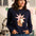 Woman wearing a navy blue sweater with a cat and star design, standing in front of a colorful wall with cat illustrations.